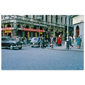 Peut inclure: Une photo vintage d'une scène de rue à Londres, en Angleterre. La photo montre un taxi noir, une boîte aux lettres rouge et plusieurs personnes traversant la rue. Le panneau au-dessus du bâtiment indique "Trumans Beers".