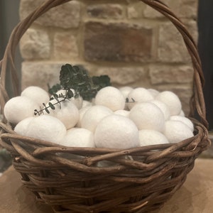 Peut inclure: Un panier en osier brun rempli de nombreuses sphères blanches. Le panier, avec une anse, est placé devant un mur de briques. Quelques brins de verdure sont nichés parmi les sphères.