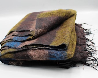 May include: A folded, rectangular blanket with a plaid pattern. The blanket features a mix of colors, including brown, blue, and yellow. The edges have a fringe. The blanket is made of a soft, fuzzy material.