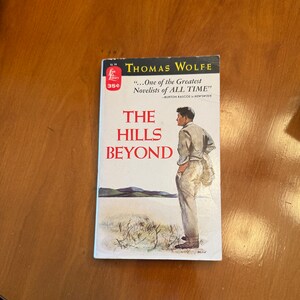 May include: A vintage paperback book cover featuring a man standing in a field with hills in the background. The book is titled "The Hills Beyond" by Thomas Wolfe. The cover also includes the quote "...One of the Greatest Novelists of ALL TIME" - Burton Rascoe in Newsweek.