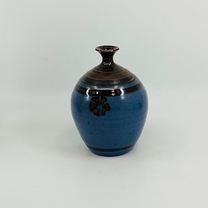 Puede incluir: Un pequeño jarrón de cerámica azul con un diseño de flor marrón y rayas marrones alrededor de la parte superior e inferior.