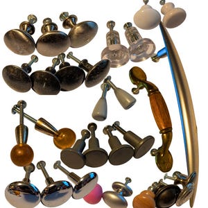 May include: A selection of cabinet knobs and pulls in various styles and materials. The collection includes metal, glass, and wood knobs, with a variety of shapes and finishes, including silver, black, and clear.
