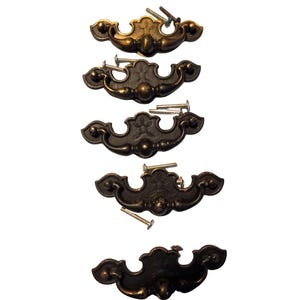 May include: Five antique-style drawer pulls in varying shades of bronze and brass. Each pull has a decorative, curved design with ornate detailing and includes mounting screws. The pulls are arranged vertically against a white background.