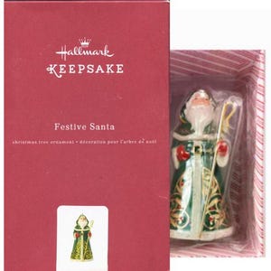 May include: A Hallmark Keepsake Christmas tree ornament featuring a Festive Santa figure. The Santa figure is dressed in a green and gold robe, holding a staff. The ornament is packaged in a red box.