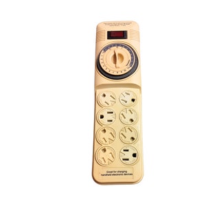 May include: A beige electrical outlet with a built-in timer. The timer has a dial with numbers 1-60 and a red LED light. The outlet has six standard three-prong outlets. The text "Great for charging handheld electronic devices" is printed below the outlets.