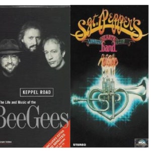 Puede incluir: Dos cintas VHS, una con una foto en blanco y negro de los miembros de la banda Bee Gees y el texto "The Life and Music of the Bee Gees" y "KEPPEL ROAD", la otra con una imagen colorida de una trompeta y el texto "Sgt. Pepper's Lonely Hearts Club Band" y "MCA".