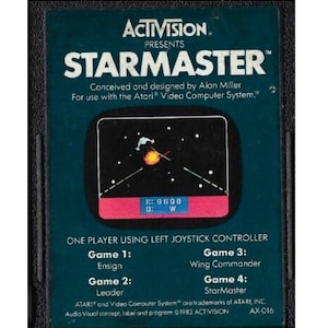 May include: A vintage Atari Starmaster video game cartridge by Activision. The dark teal cartridge features white text, including the game title and a small graphic of a spaceship firing at a target. Designed for the Atari Video Computer System.