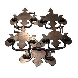 May include: A set of antique bronze drawer pulls with elaborate, floral designs. Each pull has a curved handle and decorative backplate, with screws for fitting. The hardware has a vintage, aged appearance, with a patina.