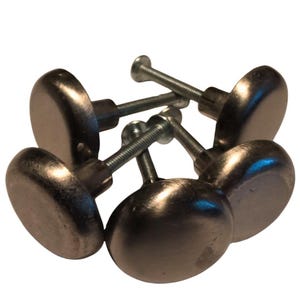 May include: Six brushed nickel cabinet knobs are shown. Each knob features a rounded, slightly domed face and a threaded screw for attachment. The knobs are arranged in a loose pile, highlighting their simple, classic design.