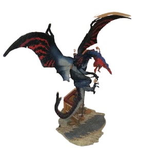 May include: A blue and red dragon figurine with black wings, standing on a rocky base. The dragon is holding a small, red and blue bird figurine in its claws.