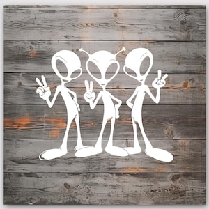 May include: White alien illustration on a wooden background. Three aliens are depicted, each with large oval heads, slender bodies, and long feet. They are making peace signs with their hands. The background is composed of weathered wooden planks.