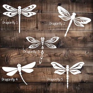 May include: Five white dragonfly designs on a wooden background. Each dragonfly has a unique wing pattern and is labeled with a number. The text "Dragonfly" is included with each design. The wood has a natural, rustic appearance.