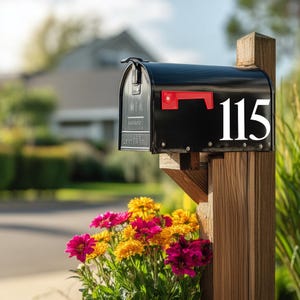 May include: A black mailbox with a red flag and the number 115 in white. The mailbox is mounted on a wooden post. Colorful pink and yellow flowers are in front of the mailbox.
