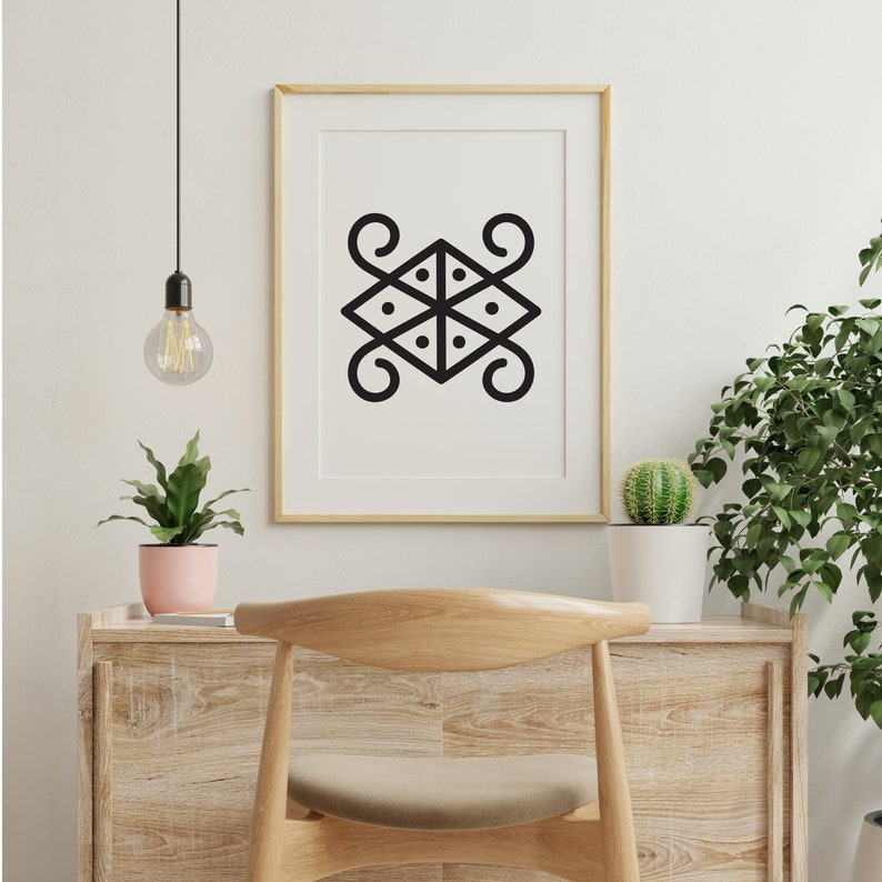 May include: A black and white geometric design print in a gold frame hanging on a white wall. The print is of a stylized symbol with four curved lines and a central square with four dots.