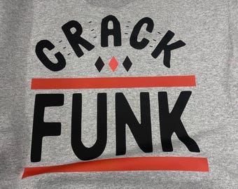 May include: A gray sweatshirt with the words "CRACK FUNK" in large black letters. The word "CRACK" is arched above the word "FUNK". A red horizontal line separates the two words. Two red diamonds are between the words.