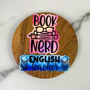May include: A wooden coaster with three colorful stickers. The top sticker reads "BOOK NERD" with glasses and books. The bottom sticker says "ENGLISH teacher" with stacks of books. The stickers have watercolor effects.