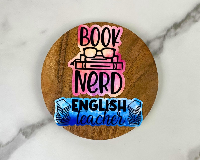 May include: A wooden coaster with three colorful stickers. The top sticker reads "BOOK NERD" with glasses and books. The bottom sticker says "ENGLISH teacher" with stacks of books. The stickers have watercolor effects.