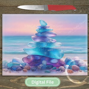 May include: A digital art print featuring a stack of colorful, translucent stones on a beach. The stones are shades of blue, purple, and pink. The background shows a sunset over the ocean. A knife with a red handle is above the print.