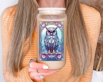 May include: A clear glass tumbler with a white lid and a colourful owl design. The owl is surrounded by a geometric frame with a blue, purple and pink colour scheme. The tumbler is being held by a person.