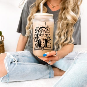 May include: A clear glass tumbler with a black and white design of headphones, flowers, and stars. The tumbler has a white lid and a straw.