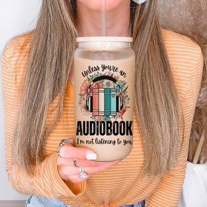 May include: A beige tumbler with a white lid and a straw. The tumbler has a floral design with headphones and books, and the text "Unless you're an audiobook I'm not listening to you".