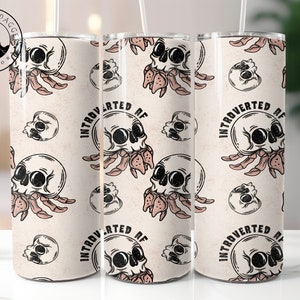 May include: Three stainless steel tumblers with a white background and a repeated pattern of a skull with a crab-like creature attached to it. The text "Introverted AF" is repeated on the tumblers.