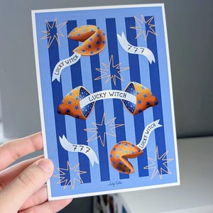 May include: A card with a blue and white striped design, showcasing illustrations of fortune cookies. The cookies are orange with blue star patterns. Text includes "LUCKY WITCH" on banners and the number "777".