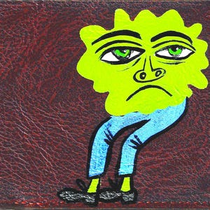 May include: A dark brown faux leather wallet featuring a hand-painted illustration of a lime green blob-shaped character with large eyes, wearing light blue trousers and black shoes, set against a textured, deep brown background surface.