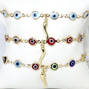 May include: Three gold chain bracelets with evil eye charms in blue, red, and green. Each bracelet has a gold horn charm.