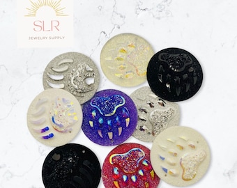 Puede incluir: Ocho abalorios redondos de resina con forma de huella de pata de oso en varios colores, incluyendo blanco, negro, morado y rojo. Cada abalorio presenta un acabado brillante y un diseño de huella de pata de oso en relieve.
