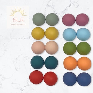 May include: A set of 12 pairs of round, colourful polymer clay earrings. The earrings are arranged in rows of two, with each row featuring a different colour. The colours include sage green, yellow, blush pink, teal, orange, and navy blue.