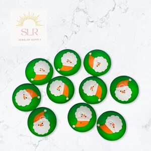 Könnte beinhalten: Zehn grüne Glascabochons mit einem Weihnachtsmann-Motiv. Jeder Cabochon zeigt einen weißen Weihnachtsmann mit roter Mütze und weißem Bart auf grünem Hintergrund.
