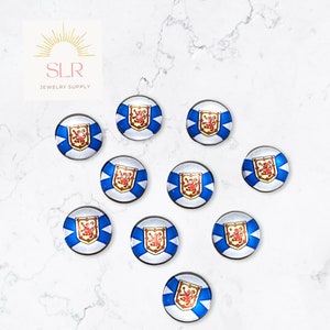 May include: Ten round glass cabochons with a blue and white design featuring the coat of arms of Nova Scotia. The cabochons are approximately 2.5 cm in diameter.