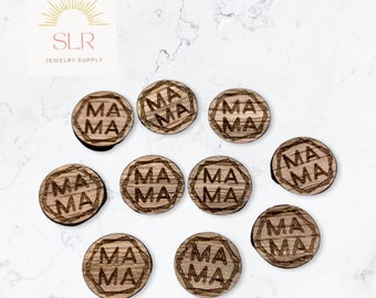 Puede incluir: Una colección de diez amuletos redondos de madera con la palabra "MAMA" grabada en una fuente decorativa. Cada amuleto es marrón con un borde oscuro y un respaldo negro. Los amuletos están dispuestos sobre una superficie de mármol blanco.