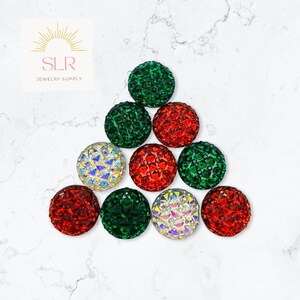 May include: A collection of 9 small, round, decorative ornaments in red, green, and iridescent colours. The ornaments are arranged in a triangle shape on a white marble surface.