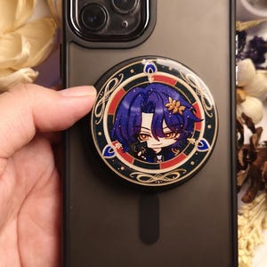 Peut inclure: Une coque de téléphone noire avec une poignée de téléphone ronde, bordée d'or, représentant un personnage de dessin animé aux cheveux violets et un motif rouge et or.