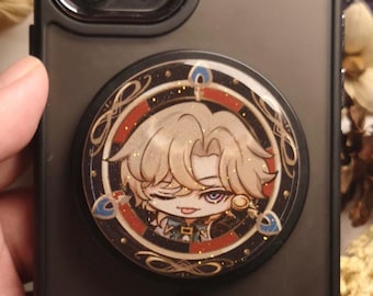 May include: A black phone case with a round, gold-rimmed pop socket featuring a cartoon character with blonde hair, a black eye patch, and a mischievous expression. The character is wearing a gold earring and a black and gold outfit.