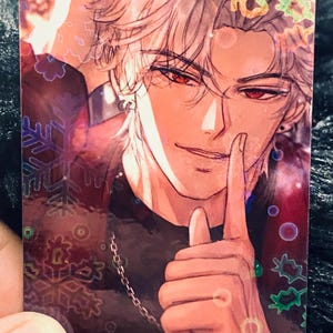 May include: A holographic trading card with an anime-style illustration of a person with silver hair and red eyes. The person is wearing a black top and a silver chain. The card has a decorative snowflake and floral design.