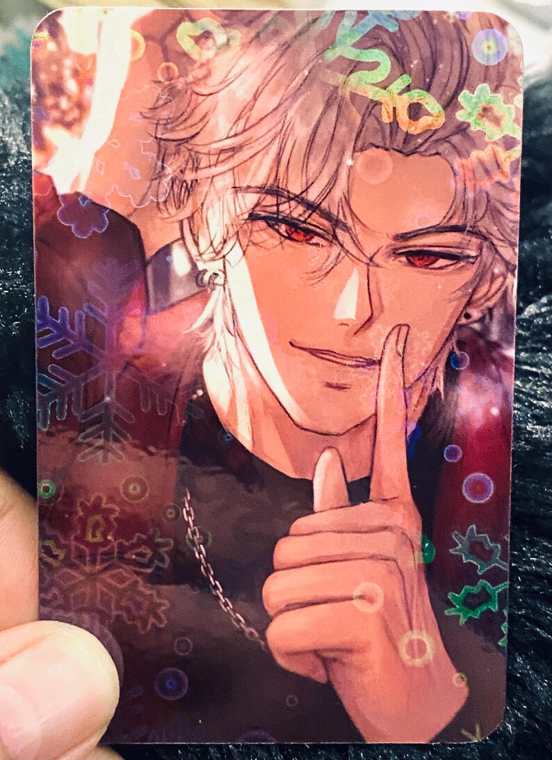 May include: A holographic trading card with an anime-style illustration of a person with silver hair and red eyes. The person is wearing a black top and a silver chain. The card has a decorative snowflake and floral design.