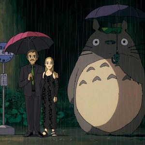 May include: An animated scene shows a couple and a large, grey creature sheltering from the rain under umbrellas. The couple stands near a bus stop sign. The creature, resembling a large cat, holds a purple umbrella.
