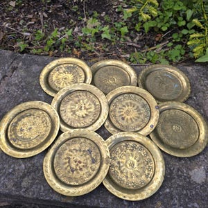 Op de afbeelding: Een verzameling antieke messing borden met ingewikkelde reliëfontwerpen. De borden variëren in grootte en patroon, met bloemen- en geometrische motieven. Het verouderde messing heeft een warme, gouden tint, wat wijst op vintage vakmanschap. Ideaal voor decoratie.