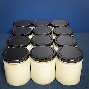 May include: A group of 12 clear glass jars with black lids filled with a white substance. The jars are arranged in a rectangular pattern on a blue surface.