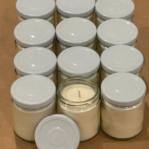 May include: A group of 10 small glass jars with white lids filled with white candle wax. One jar has a lit candle wick.