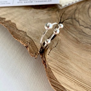 Könnte beinhalten: Ein silberner Ring mit vier runden, strukturierten Silberperlen. Der Ring liegt auf einer Holzoberfläche.