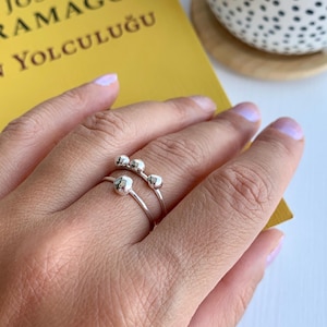 Könnte beinhalten: Ein silberner Ring mit drei runden, strukturierten Perlen auf einem dünnen Band. Der Ring wird an einem Finger getragen.