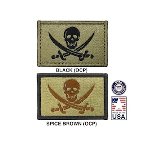 Könnte beinhalten: Zwei gestickte Patches mit einem Totenkopf- und Knochenkreuz-Motiv. Der obere Patch ist schwarz auf einem braunen Hintergrund. Der untere Patch ist braun auf einem braunen Hintergrund. Beide Patches haben den Text "BLACK (OCP)" und "SPICE BROWN (OCP)" darunter.