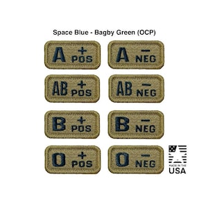 Könnte beinhalten: Acht gestickte Aufnäher mit Blutgruppenbezeichnungen: A+, A-, AB+, AB-, B+, B-, O+, und O-. Die Aufnäher sind rechteckig mit beigem Hintergrund und dunkelblauen Buchstaben. Der Text "MADE IN THE USA" ist ebenfalls sichtbar.