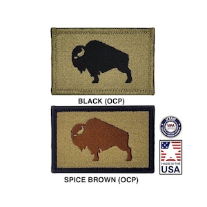 Może przedstawiać: Dwa haftowane naszywki przedstawiające czarną i brązową sylwetkę bizony na beżowym tle. Naszywki są oznaczone jako "BLACK (OCP)" i "SPICE BROWN (OCP)".
