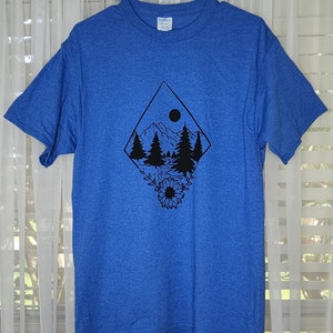 Peut inclure: Un t-shirt bleu royal chin&eacute; avec un motif graphique noir repr&eacute;sentant une sc&egrave;ne de montagne avec une lune, des arbres et un tournesol. Le texte "Front" est visible dans le coin sup&eacute;rieur droit de l'image.