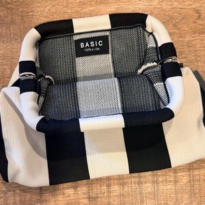 May include: A black and white striped handbag with a rectangular shape. The bag has a handle and a label that reads "BASIC 100% a vibe". The bag is made of a woven material.